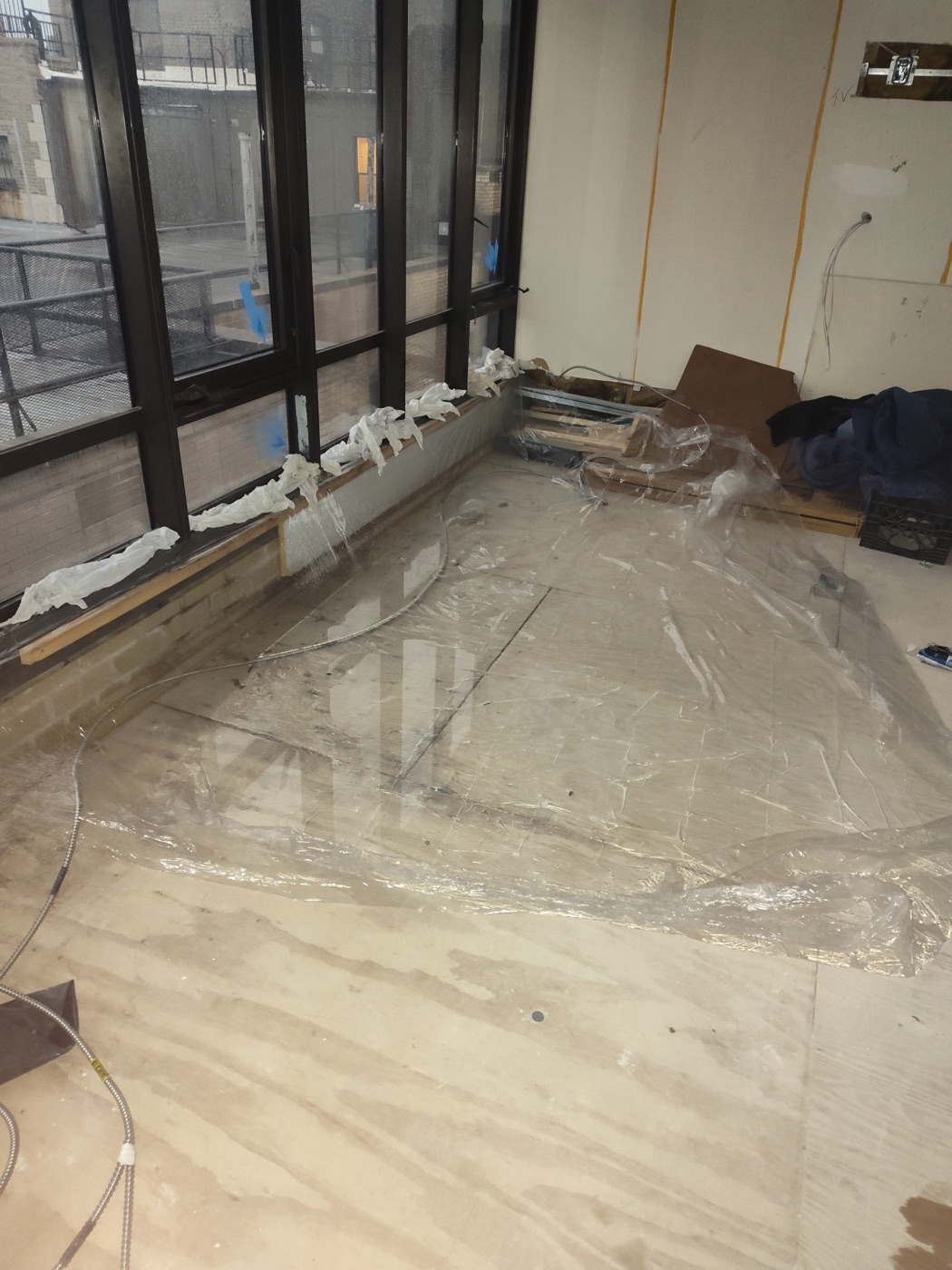 Towels lining the window sills and plastic sheeting covering a water-stained floor below the windows